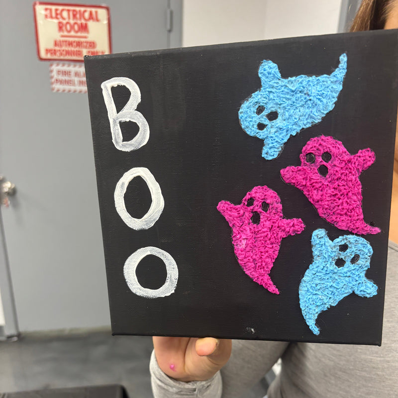 Decorative sign with crocheted ghosts and 'BOO' text held by a person.